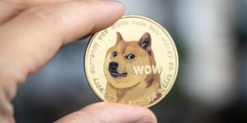 Dogecoin cryptocurrency physical coin held between two fingers.