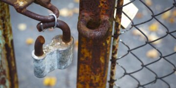 Rusty lock cut open and hanging on an open, rusty gate