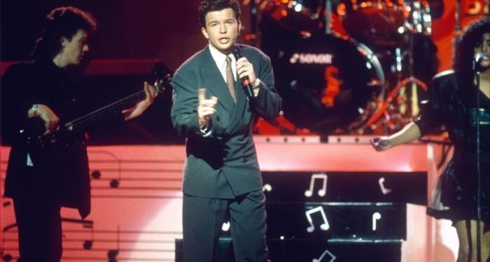 A man in a suit sings into a microphone on stage