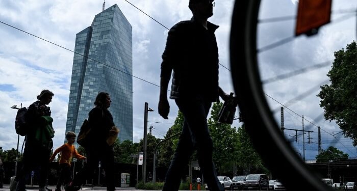 People cross a street in front of the headquarters building of the European Central Bank in Frankfurt