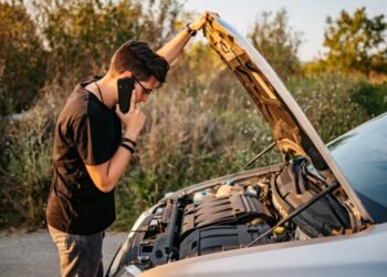 Adult looking at open hood of car and calling roadside assistance