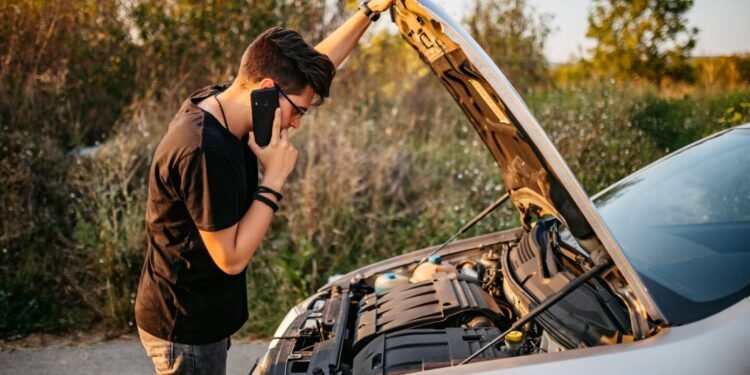 Adult looking at open hood of car and calling roadside assistance