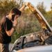 Adult looking at open hood of car and calling roadside assistance