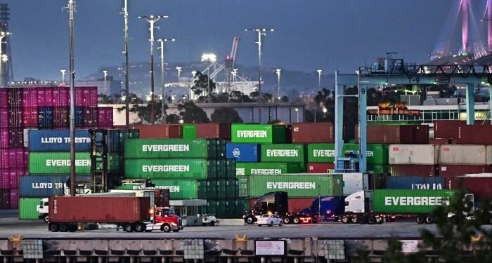 Container trucks driving past stacks of shipping containers at the Port of Los Angeles