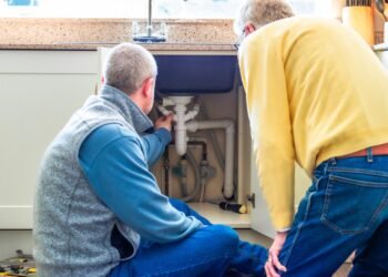 Two people looking at pipes under a sink.