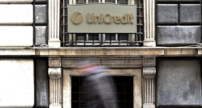 A person walks past a sign with the logo of the Italian bank UniCredit on its bank branch in central Genoa,