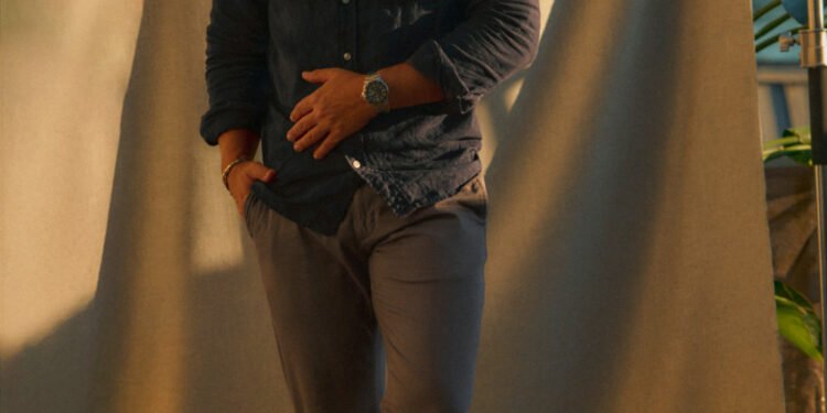 andrew wearing a blue linen shirt, stone chinos, brown loafers, a watch and sunglasses