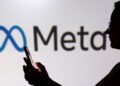 A person holding a smartphone is silhouetted in front of a large Meta logo.
