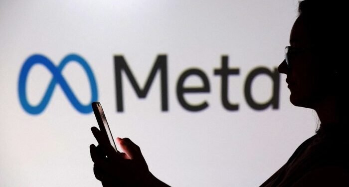 A person holding a smartphone is silhouetted in front of a large Meta logo.