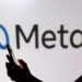 A person holding a smartphone is silhouetted in front of a large Meta logo.