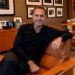 Gerry Cardinale sits in a brown leather chair in an office decorated with framed photos and shelves of memorabilia.