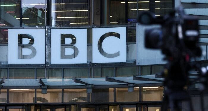 The BBC logo displayed on the exterior of BBC Broadcasting House with a television camera in the foreground.