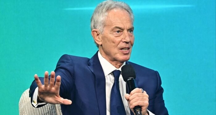 Tony Blair speaks into a microphone and gestures with his hand during a panel discussion.